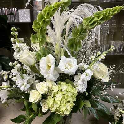 Tall white floral arrangement with green accents in a clear vase