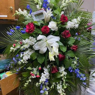 Large standing floral spray with red roses, white lilies, and blue flowers