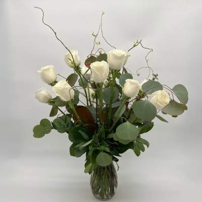 Tall arrangement of white roses with curly branches in a clear glass vase