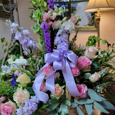 Basket arrangement of pink and lavender roses with a purple ribbon