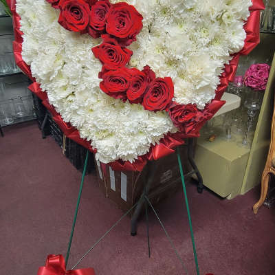 Heart-shaped floral tribute with white chrysanthemums and red roses on a stand