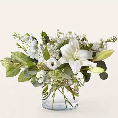 Low glass vase of white lilies and blooms with assorted foliage