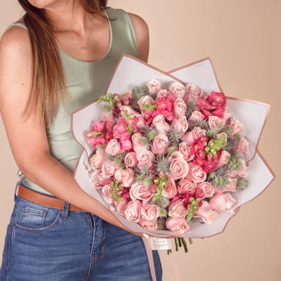 Woman holding a large bouquet of pink roses and snapdragons wrapped in white paper