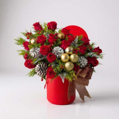 Red roses arranged in a red vase with gold ornaments and pinecones