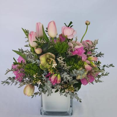 Pink tulips and mixed blooms arranged in a clear square vase