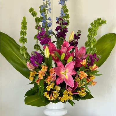 Tall mixed bouquet of lilies and purple flowers in a white pedestal vase