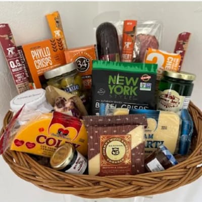 Gift basket filled with assorted snacks, cheeses, and jars in a wicker basket