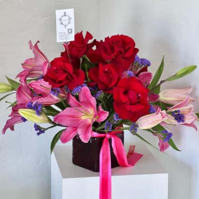 Red roses and pink lilies in a dark vase with a pink ribbon