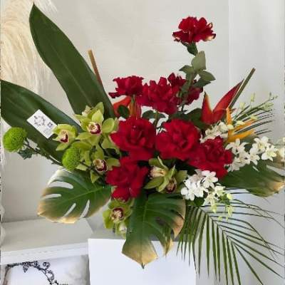 Red roses and green orchids arranged with tropical leaves in a white vase.