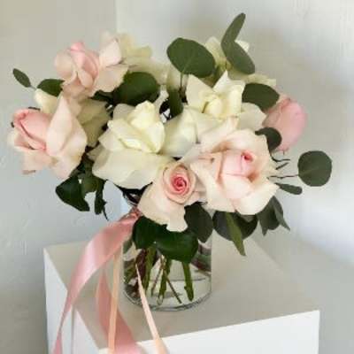 Bouquet of pale pink and white roses in a glass vase with a pink ribbon