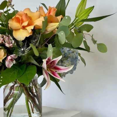 Bouquet of peach roses, lilies, and blue hydrangea in a glass vase