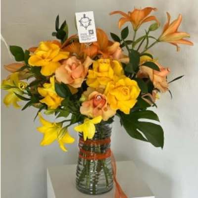 Orange and yellow lilies arranged in a glass vase with ribbon