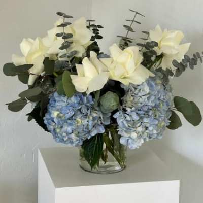 Blue hydrangeas and white flowers in a clear glass vase