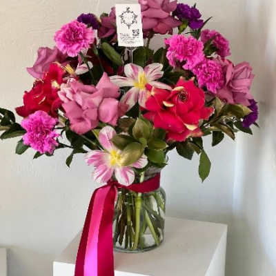 Pink and red mixed flower bouquet in a glass vase with a ribbon