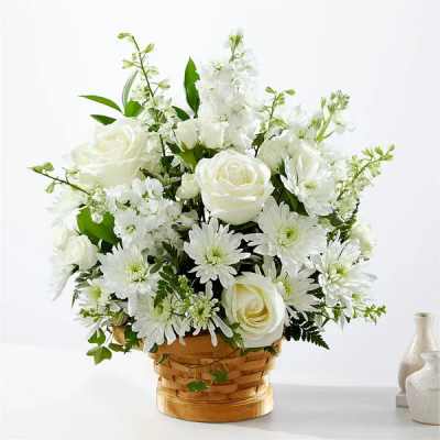 White roses and mums arranged in a woven basket with soft white filler flowers
