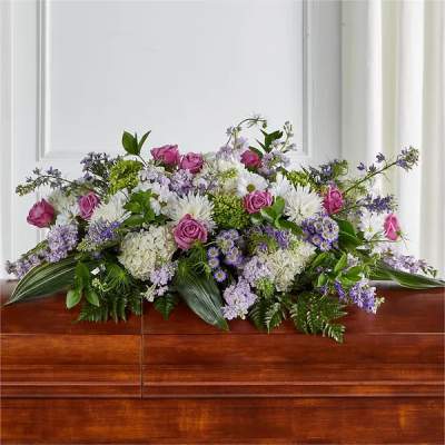 Lavender, pink, and white casket spray with roses, mums, hydrangeas and asters on a wooden casket