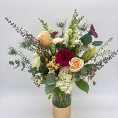Tall mixed arrangement with peach roses, fuchsia gerbera daisies, white hydrangeas and snapdragons in a glass vase