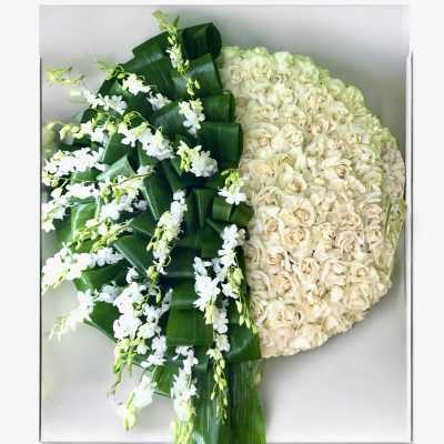 Round cream rose arrangement with cascading white orchids and dark green leaves