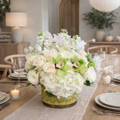 White floral centerpiece in a gold vase on a dining table
