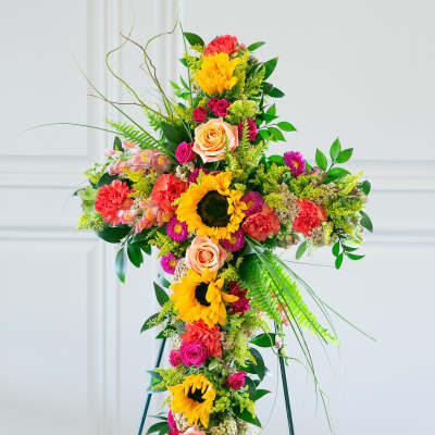 Standing floral cross with bright sunflowers, roses, and mixed blooms on an easel