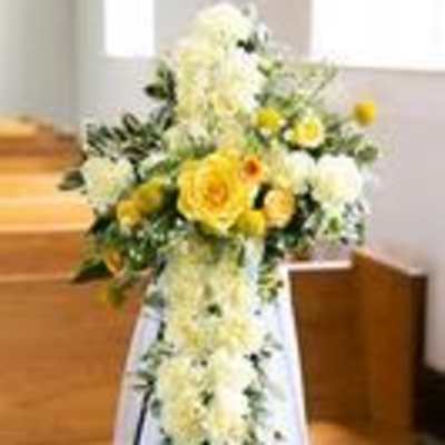 Standing cross-shaped arrangement of white and yellow flowers on an easel in a church aisle
