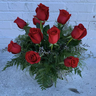Red roses arranged in a clear glass vase with greenery