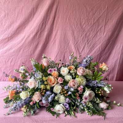 Large pastel bouquet of roses, lavender blooms, and mixed flowers on pink fabric