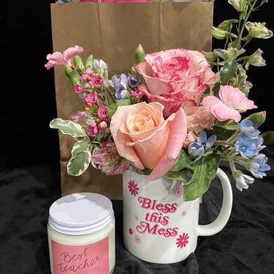 Pink and peach flower arrangement in a mug with a candle beside it
