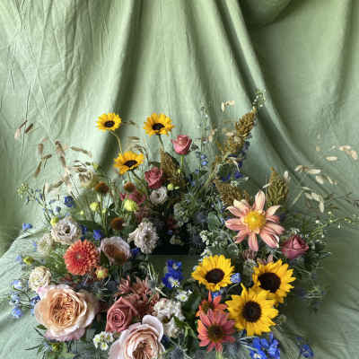 Mixed bouquet with sunflowers, roses, and pastel blooms on green fabric