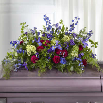 Long spray of purple, blue, green, and red flowers arranged on top of a closed casket
