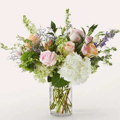Mixed bouquet of pink and peach roses, white hydrangea, and accents in a clear glass vase