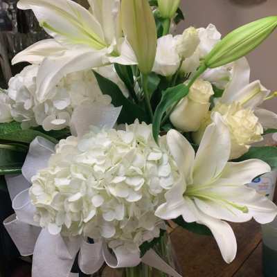 White lilies and hydrangeas in a clear glass vase with a white ribbon