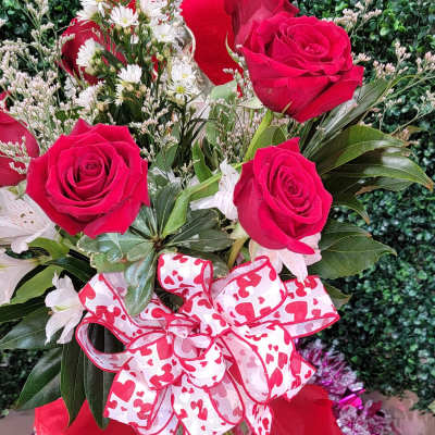 Bouquet of red roses and white daisies in a glass vase with a heart ribbon