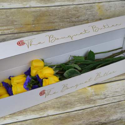 Yellow roses with purple filler in a white bouquet box