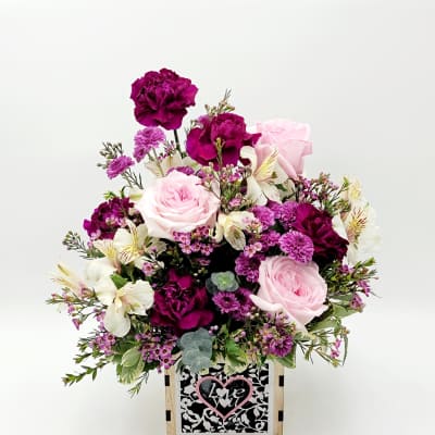 Pink and purple floral arrangement in a wooden box with a heart sign