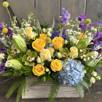 Mixed bouquet with yellow roses, purple flowers, and blue hydrangea in a wooden box