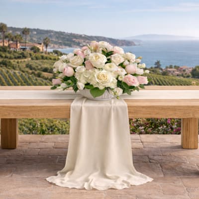 White and blush rose arrangement on a draped table outdoors