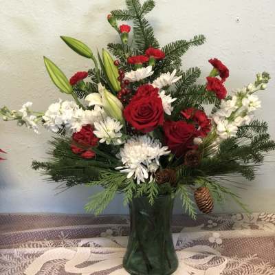 Red roses and white flowers in a green glass vase with pine accents