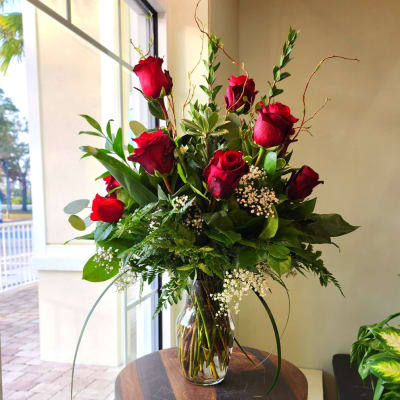 Tall arrangement of red roses with white filler flowers in a clear glass vase