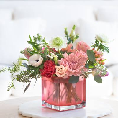 Low pink and white mixed flower arrangement in a pink glass cube vase on a light table