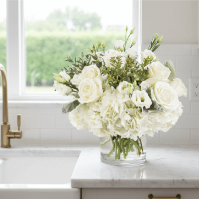 White roses and hydrangeas arranged in a clear glass vase on a marble countertop.