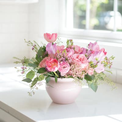 Low pink arrangement of tulips, roses, and ranunculus in a pale pink ceramic bowl