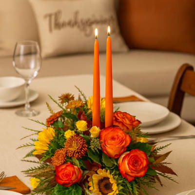 Table centerpiece with orange candles and mixed flowers on a dining table