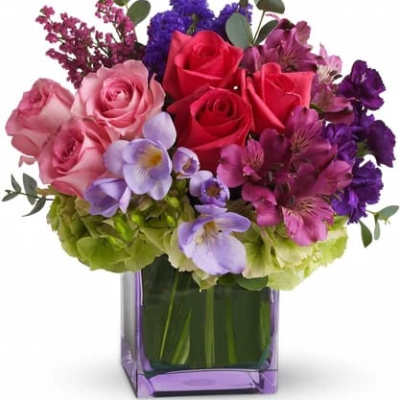 Mixed bouquet of roses, hydrangeas, and purple flowers in a square vase