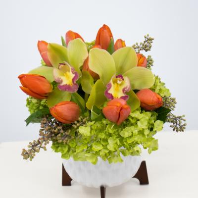 Orange tulips and green orchids in a white vase