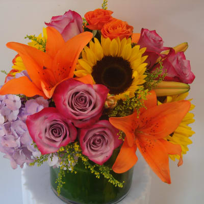Mixed bouquet with roses, lilies, sunflower, and hydrangea in a glass vase
