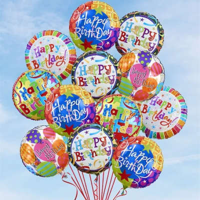Cluster of colorful round Happy Birthday balloons with red ribbons against a blue sky