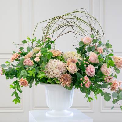 Large blush and peach flower arrangement in a white urn with arching branches