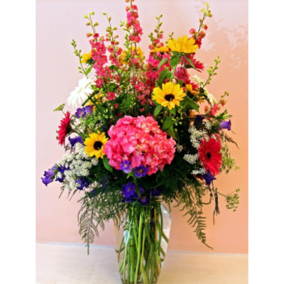 Tall mixed bouquet in a clear glass vase with pink, yellow, red, white, and purple flowers