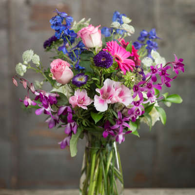 Mixed bouquet of pink, purple, and blue flowers in a clear glass vase